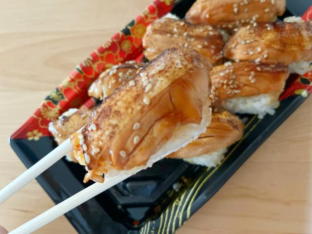 ロピアのオリジナル、炙りサーモン寿司を箸で持ち上げる