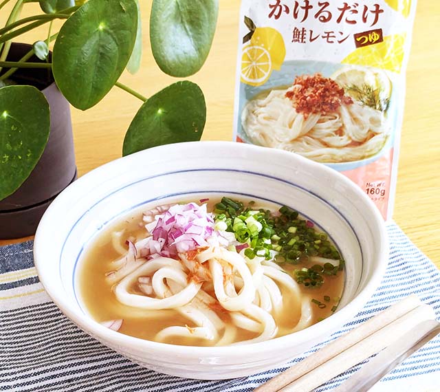 カルディ「麺にかけるだけ　鮭レモンつゆ」のパッケージと、カルディ「麺にかけるだけ　鮭レモンつゆ」をかけたうどんがテーブルに並んでいる様子