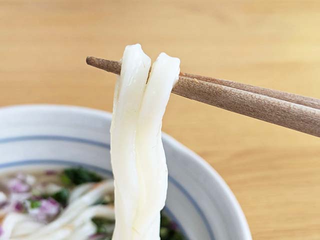 カルディ「麺にかけるだけ　鮭レモンつゆ」をかけたうどんの麺を箸で持ち上げているところ