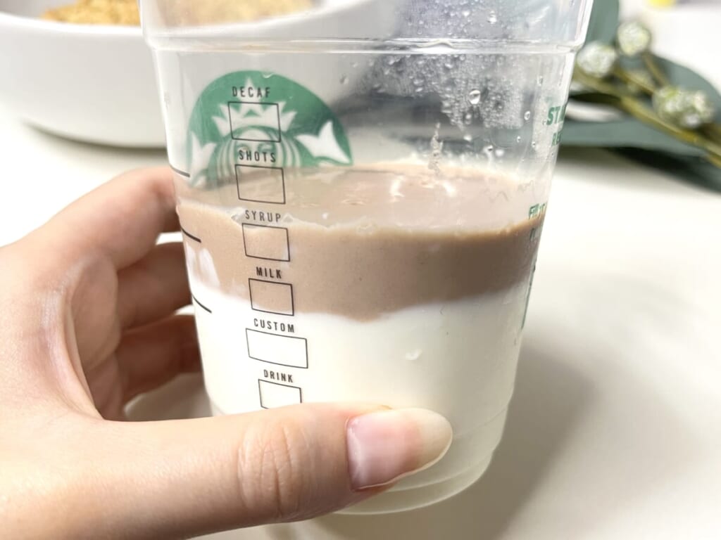 スターバックスコーヒーのカップを手に持ち、カルディ「パンダ杏仁豆腐 ミニ」を加熱して溶かしたプレーンとココア風味を2層に重ねて冷やし固めた様子