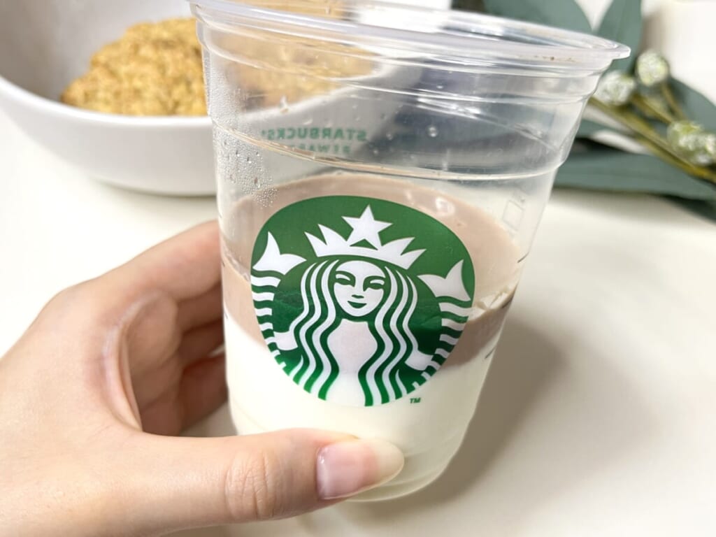 スターバックスコーヒーのカップを手に持ち、カルディ「パンダ杏仁豆腐 ミニ」を加熱して溶かしたプレーンとココア風味を2層に重ねた様子