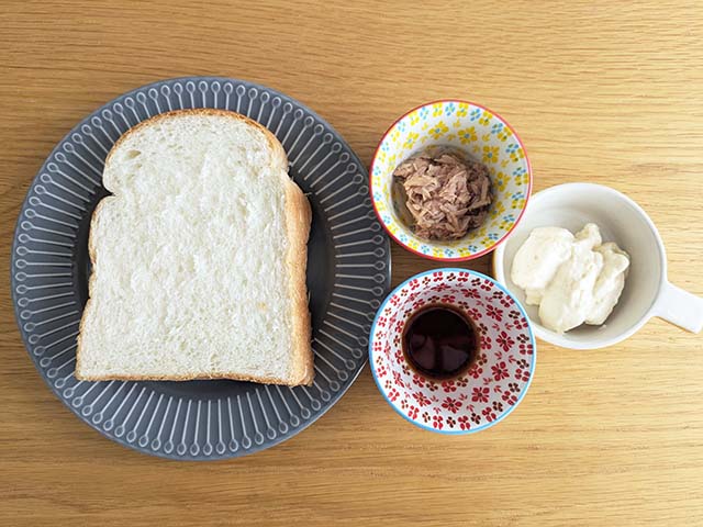 ツナマヨトーストの材料、ツナ　1/2缶、マヨネーズ　大さじ2、醤油　小さじ1/2、食パン1枚がテーブルに並んでいる様子