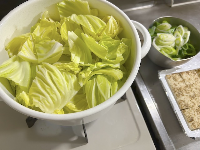 もつ鍋の調味料とキャベツ、水を入れた鍋と刻んだネギ、焼き豆腐。