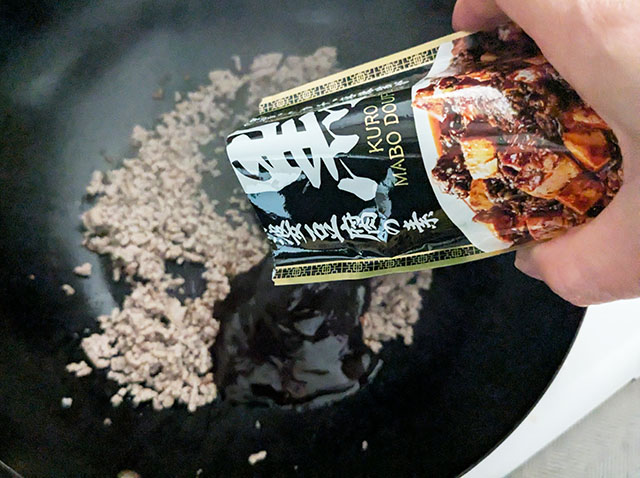 フライパンで炒めた合挽肉にカルディ「黒麻婆豆腐の素」をかけている様子