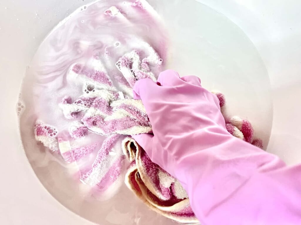 スニーカーを入れたランドリーバケツで「オキシクリーン」の溶液を作り、手で揉み込みオキシ漬けしている様子