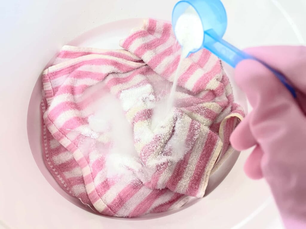 タオルを入れたランドリーバケツで「オキシクリーン」の溶液を作る様子