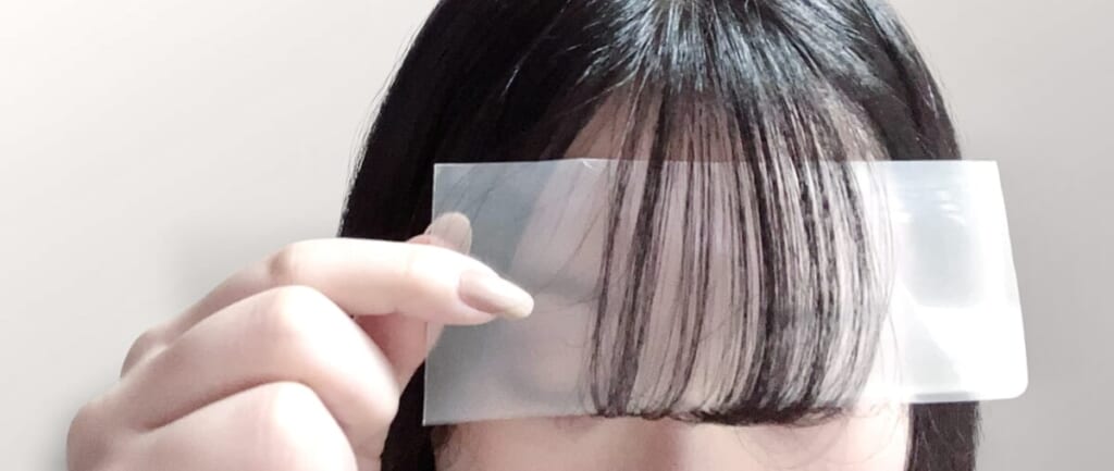 小さく切ったクリアファイルで前髪をセットしている様子