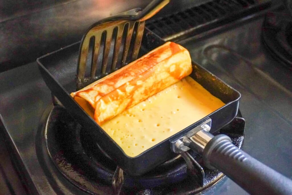 卵焼き器に生地を入れ、バナナと一緒に巻いているようす