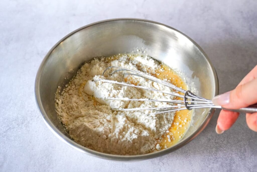 ボウルに卵、牛乳、はちみつ、ホットケーキミックス入れ泡だて器で混ぜているようす