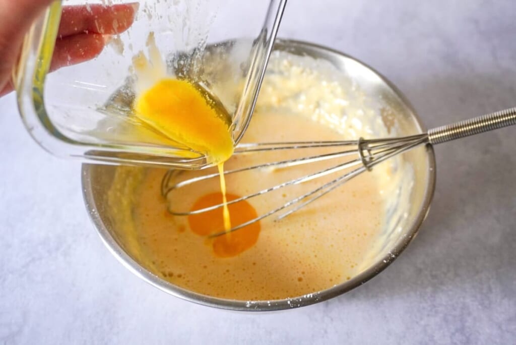 ボウルに卵、牛乳、はちみつ、ホットケーキミックス入れて混ぜ、耐熱容器で溶かしたバターを加えているようす