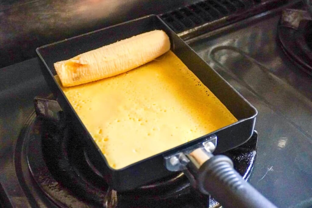 卵焼き器に生地を入れ、端にバナナを置き焼いているようす