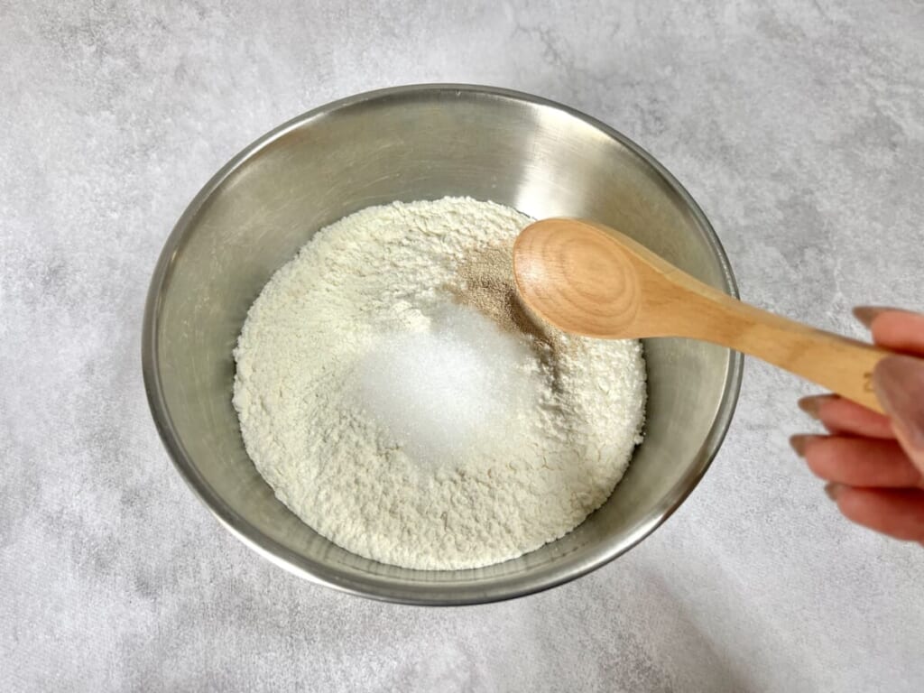 ボウルに強力粉、ドライイースト、グラニュー糖を入れ、スプーンで混ぜている様子