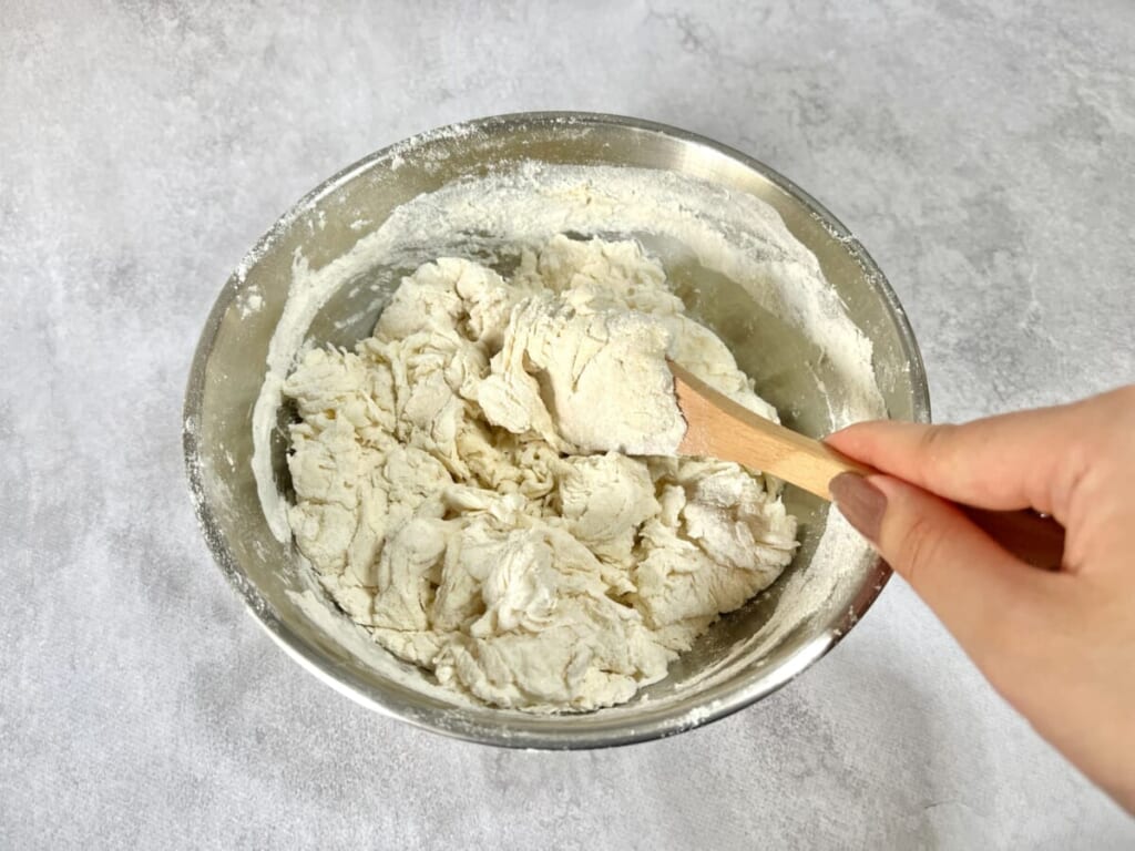 ボウルに強力粉、ドライイースト、グラニュー糖を入れ、ぬるま湯を注いでスプーンで混ぜている様子