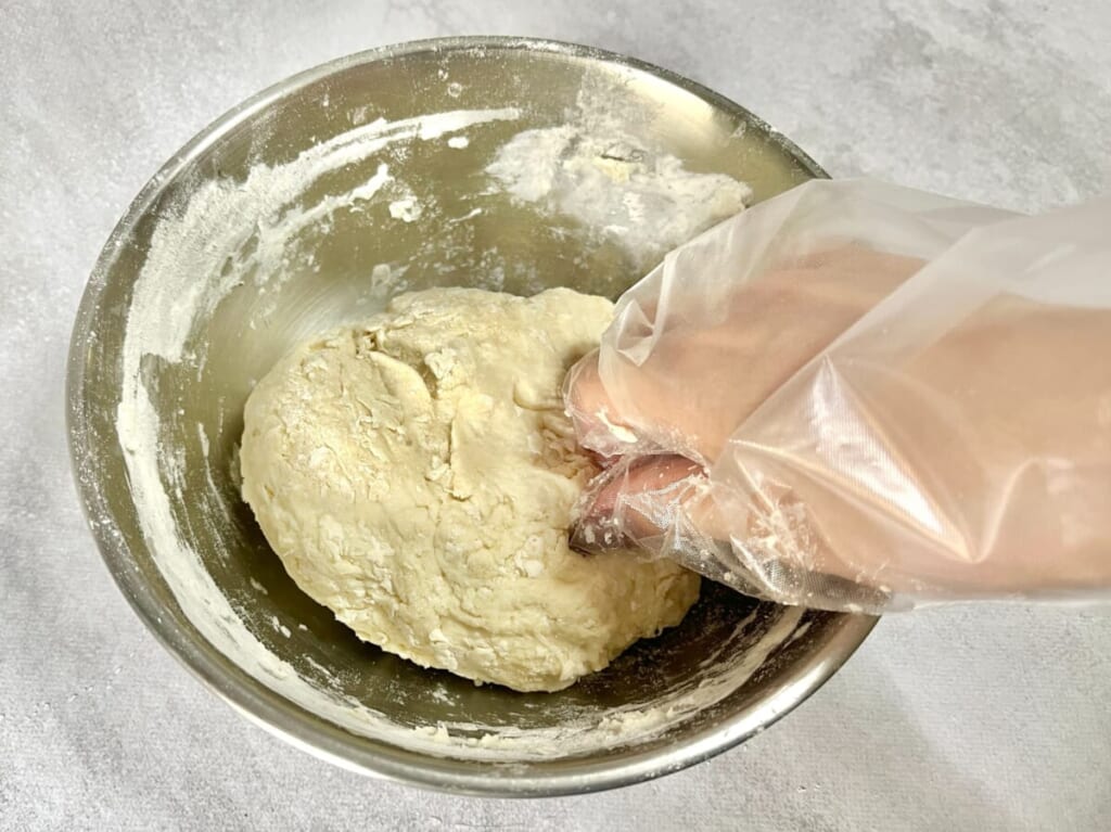 ボウルで混ぜた生地にバターを加え、手でこねている様子