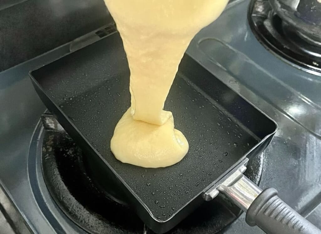 卵焼き器にサラダ油を引き、チーズドッグの生地を流し込んでいる様子