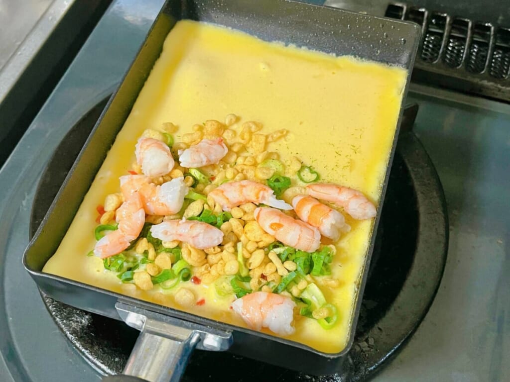 卵焼き器に「カクたこ」の生地を入れ、薬味ねぎ、天かす、紅しょうが、蒸しえびを加えた様子