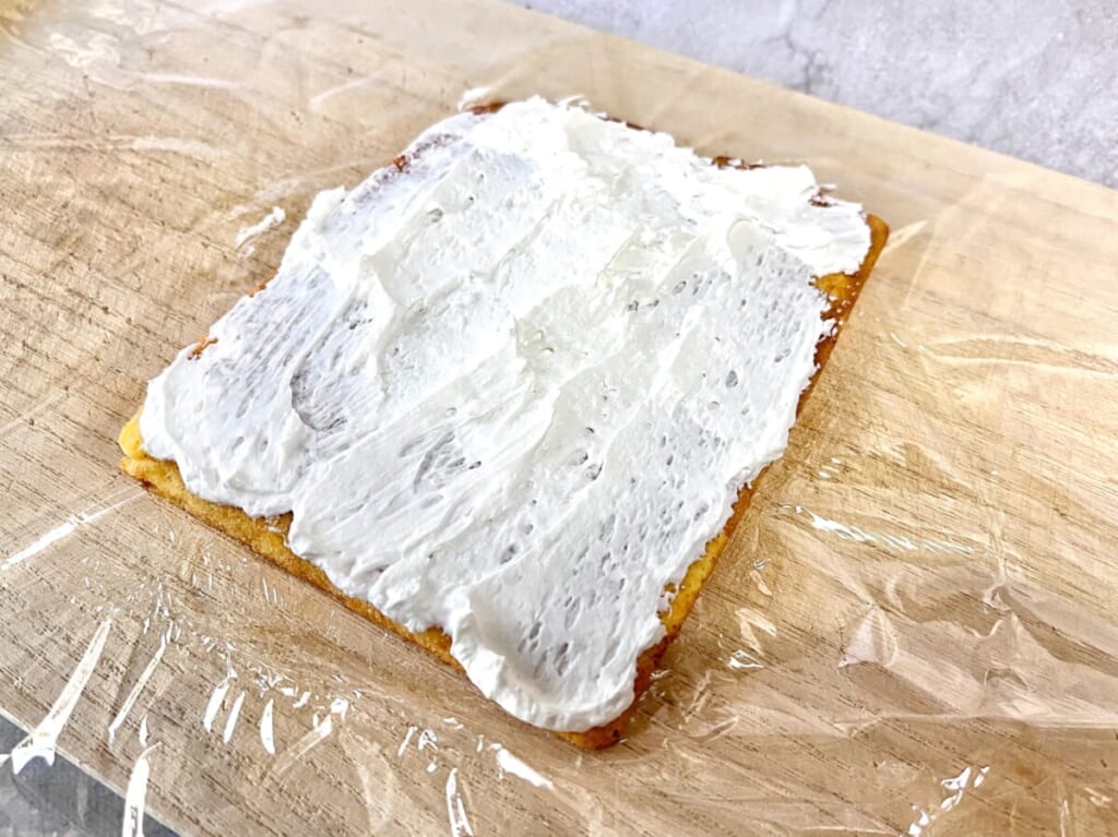 まな板の上にキッチンラップを敷き、「いちごのキャンドルケーキ」の生地にホイップクリームを塗り広げた様子